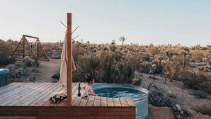 Um deck de madeira com hidromassagem, uma pérgola e paisagem desértica ao fundo.
