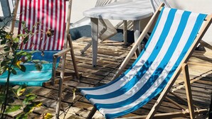 Un patio con dos sillas de playa a rayas, una mesa blanca y una ventana.