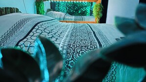 Una cama con una colcha estampada, un cabecero de madera y una pared con un panel verde texturizado y dos plantas en macetas.