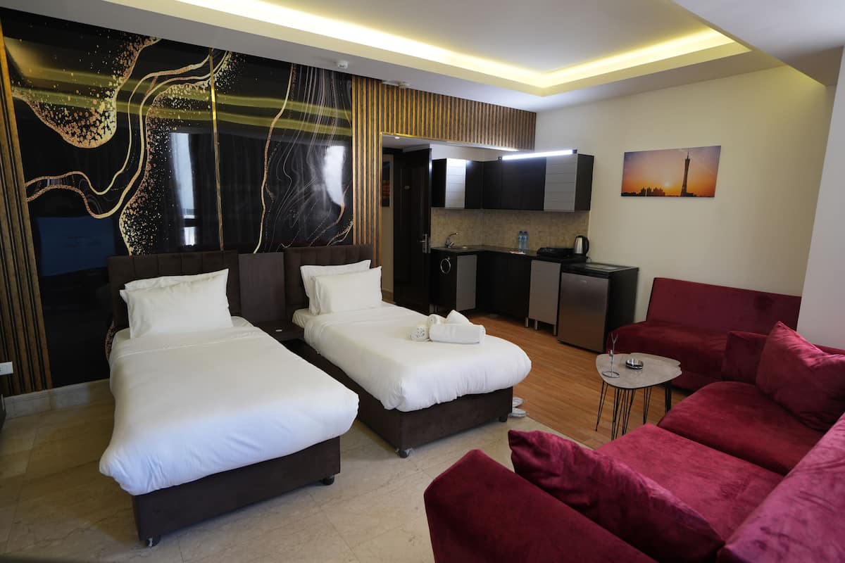 Et moderne hotelværelse med to senge, en rød sofa, et lille bord, et fjernsyn og et tekøkken.