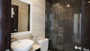 Un baño moderno con un lavamanos blanco, un espejo grande, un inodoro y una zona de ducha con mampara de vidrio.