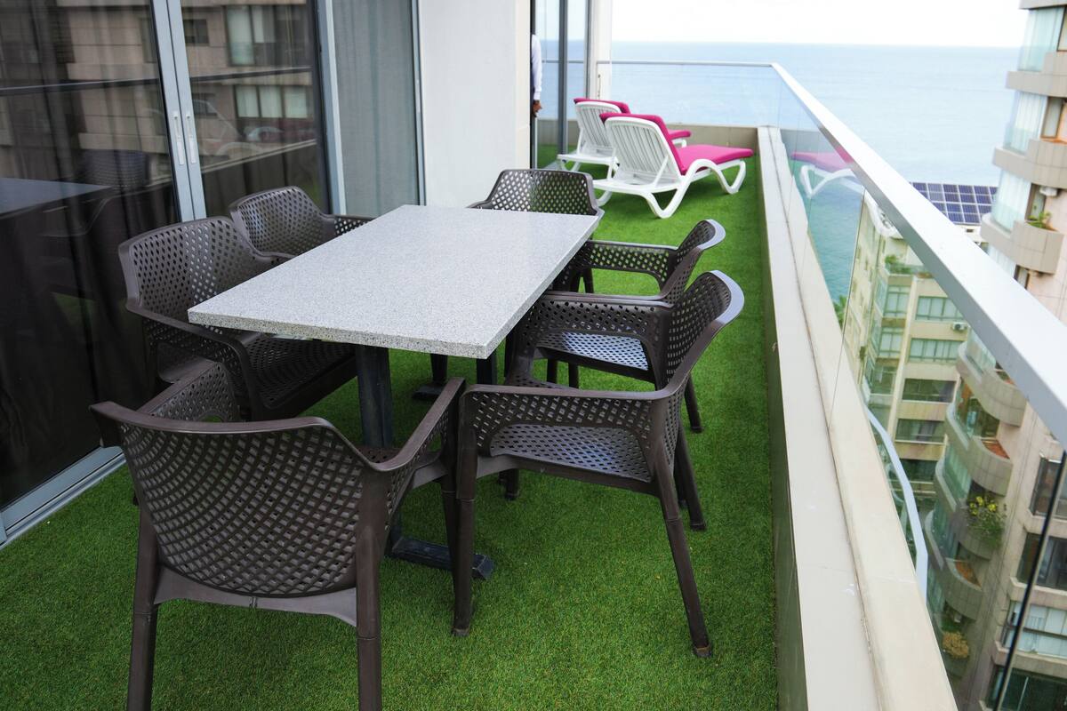 En balkon med et bord og stole, et rødt markise og udsigt til havet.