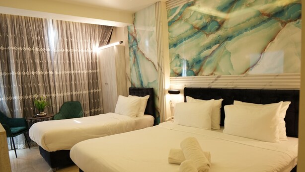 Habitación de hotel con dos camas, una silla verde, una mesita con una planta y un muro de mármol.