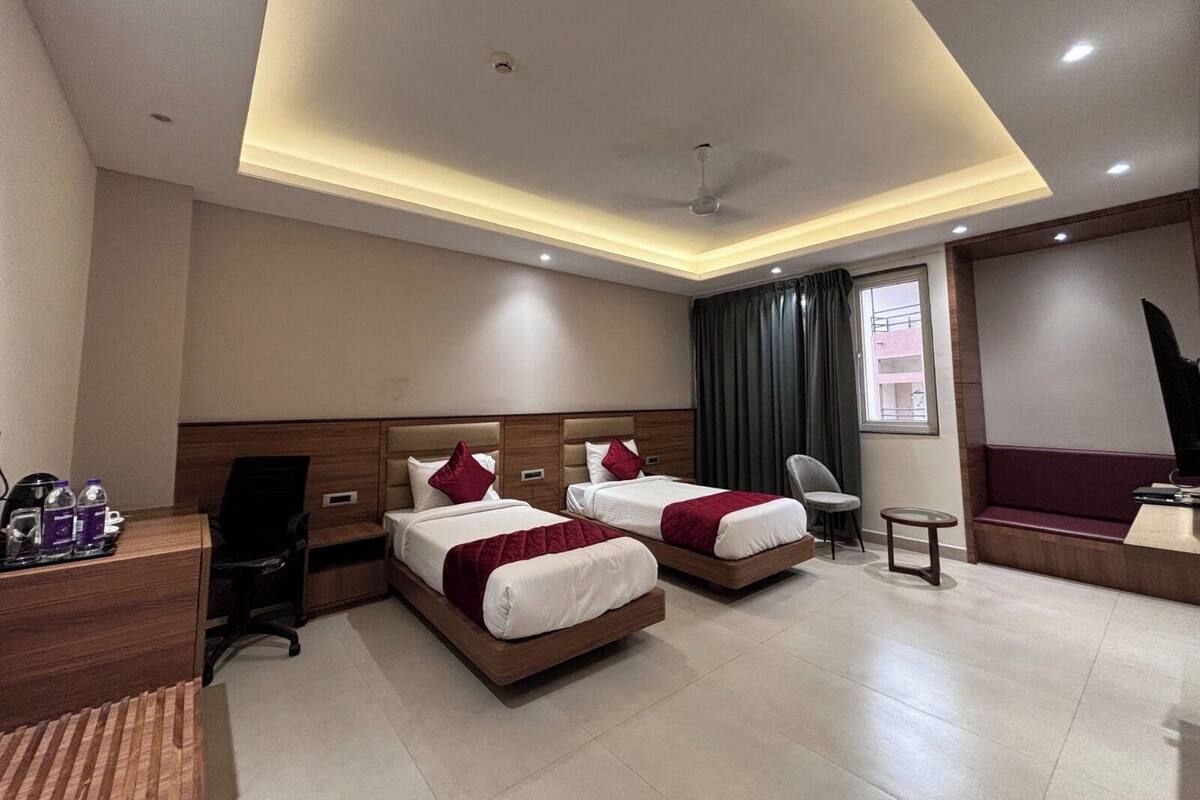 A hotel room with two beds, a desk, a chair, a small table, and a TV.
