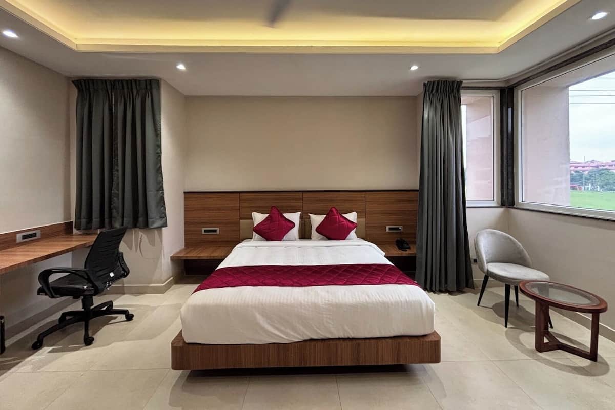 A hotel room with a large bed, a desk, a chair, a small table, and a window with curtains.