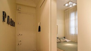 A bedroom with a bed, a window with curtains, and a door with a coat hanging on it. - Le Marais Moderne (Paris)