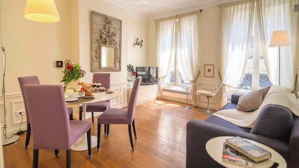 A living room with a sofa, dining table, chairs, and a TV. - Le Marais Moderne (Paris)