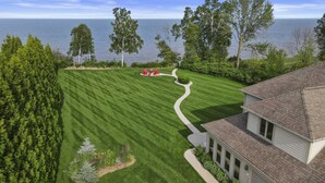 Une pelouse bien entretenue, avec un sentier sinueux menant à un espace de détente, entourée d’arbres et offrant une vue sur la mer.
