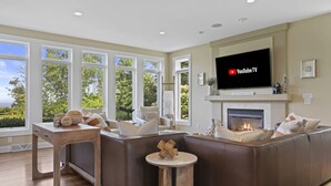 Un salon moderne doté d’une cheminée, d’un grand téléviseur et offrant une vue sur l’extérieur.