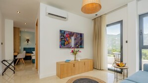A modern living room with a sofa, a coffee table with fruit, a painting on the wall, and a view through a glass door. - Hotel Aquilo (Petrovac)