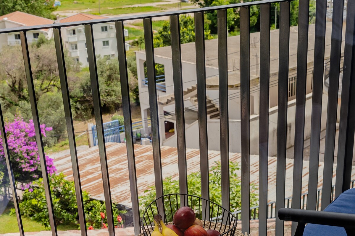 A balcony with a metal railing overlooking a residential area with houses and a road.