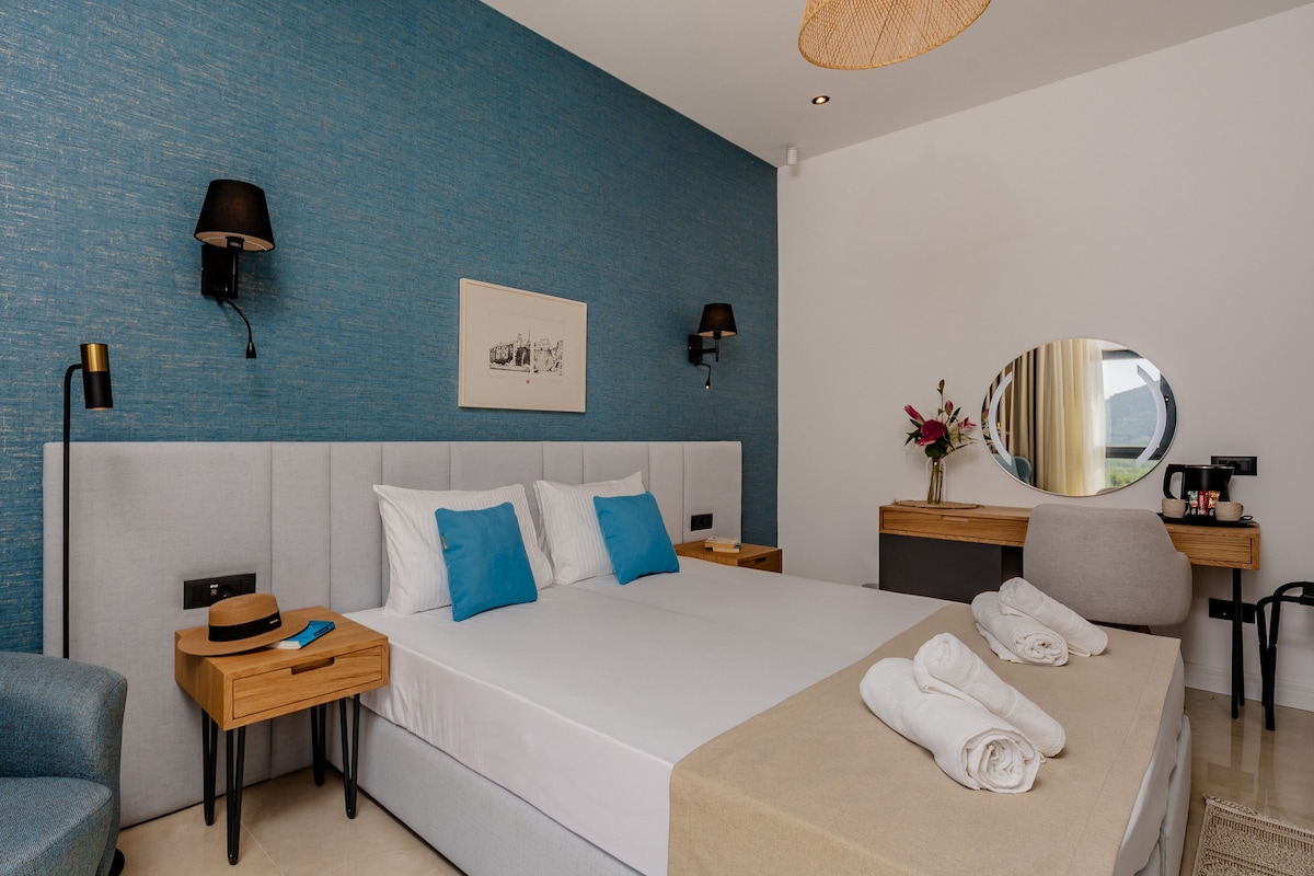 A modern hotel room with a large bed, a desk, a chair, and a nightstand.