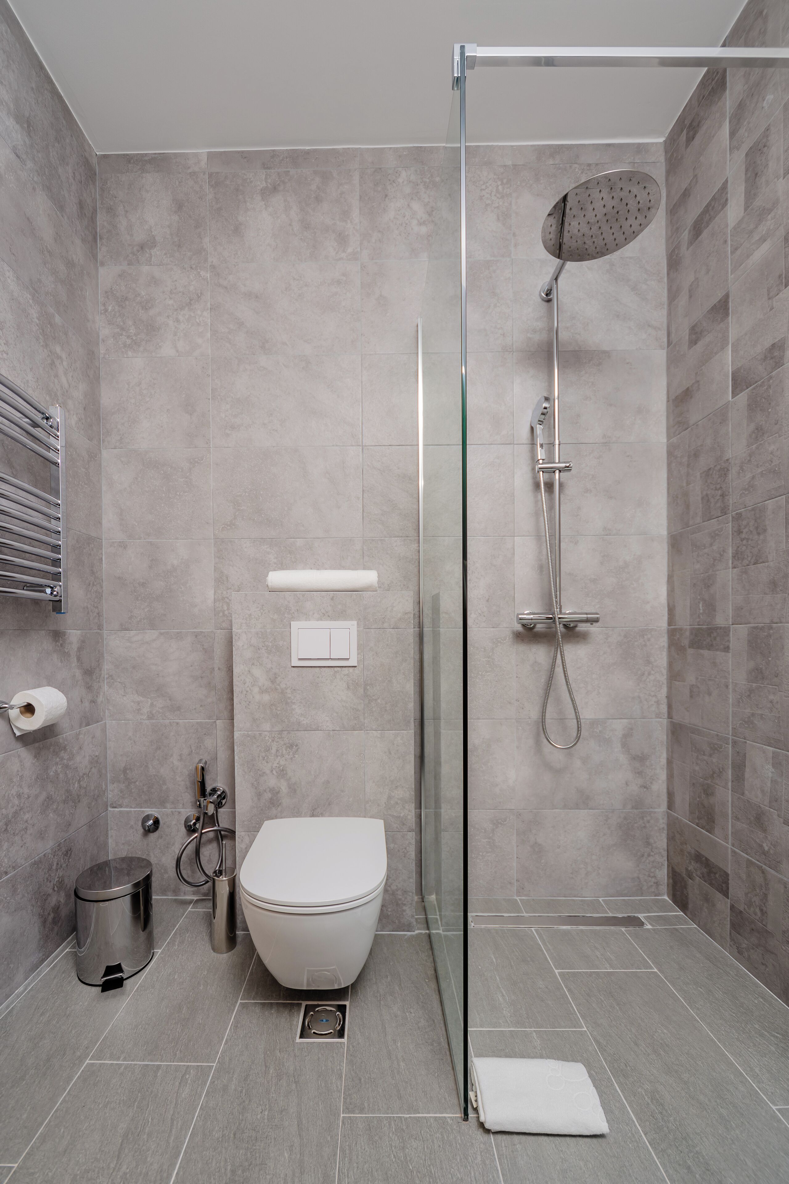 A modern bathroom with a glass-enclosed shower, a white toilet, and a stainless steel trash can.