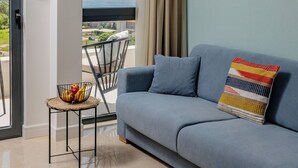 A modern living room with a blue sofa, a wicker pendant light, a small table with fruit, and a view of the sea through large windows. - Hotel Aquilo (Petrovac)