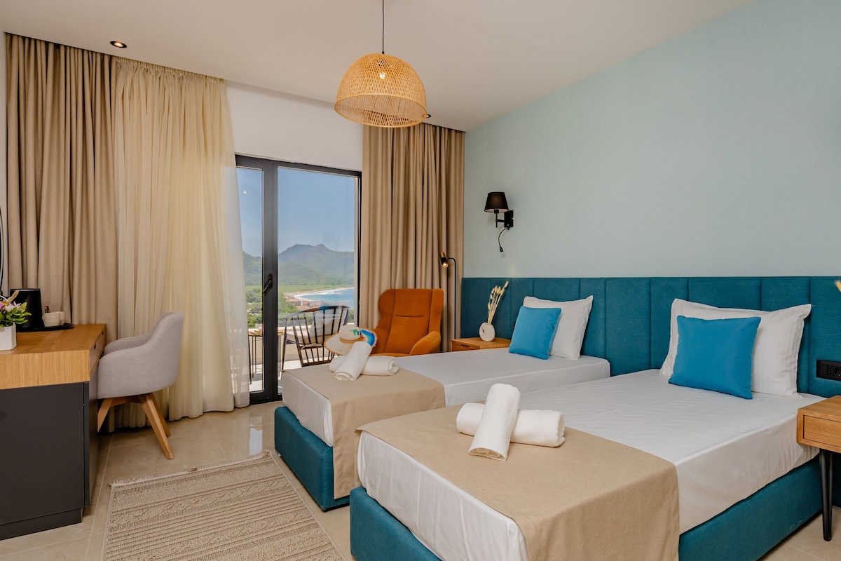 A hotel room with two beds, a desk, a chair, and a view of the mountains.