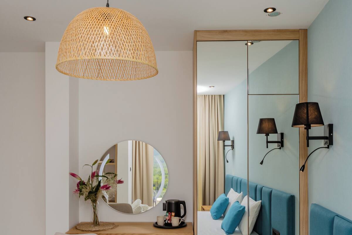 A hotel room with a bed, a desk, a chair, a mirror, and a hanging light fixture.