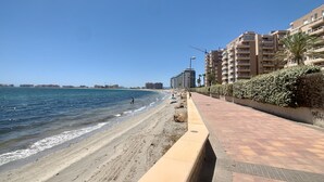 A beachside promenade with a clear sky, a calm sea, and residential buildings in the background. - Bright and fully equipped in a front line development (La Manga del Mar Menor)