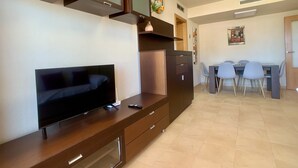 A modern living room with a flat-screen TV, wooden cabinets, and a dining area with a table and chairs. - Bright and fully equipped in a front line development (La Manga del Mar Menor)