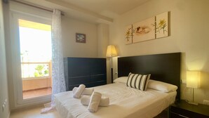 A hotel room with a bed, a TV, a nightstand, a lamp, and a window with a view of the outside. - Bright and fully equipped in a front line development (La Manga del Mar Menor)