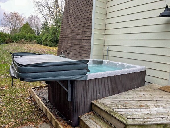 Un bain à remous avec un couvercle, des marches en bois et une maison en arrière-plan.