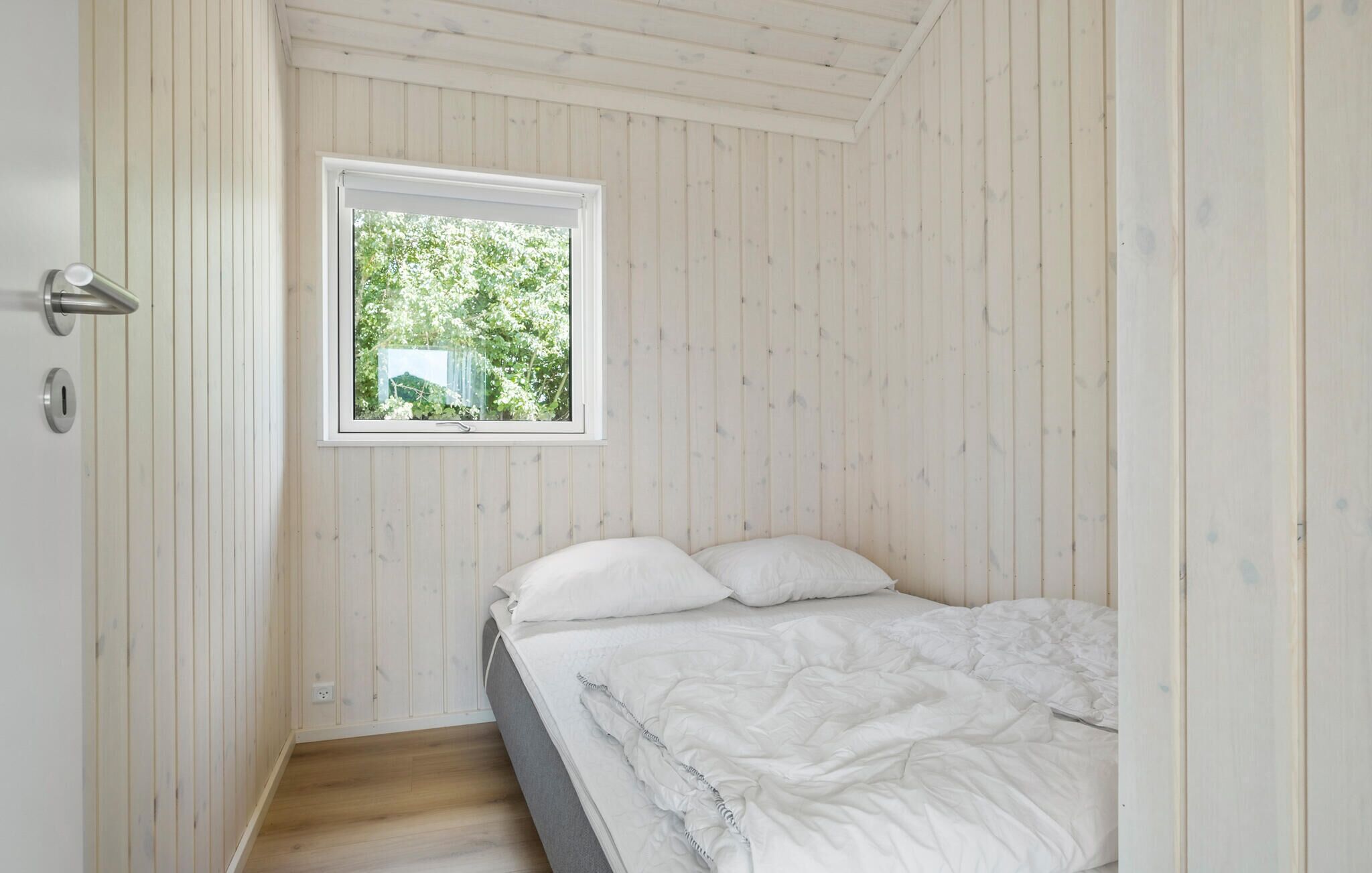 Un dormitorio con una cama individual, una ventana con vistas a la vegetación y paneles de madera en las paredes.