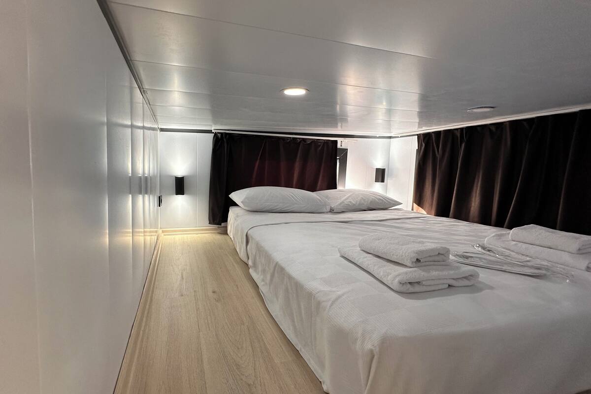 A modern hotel room with a neatly made bed, a bedside table, and a wall-mounted light fixture.