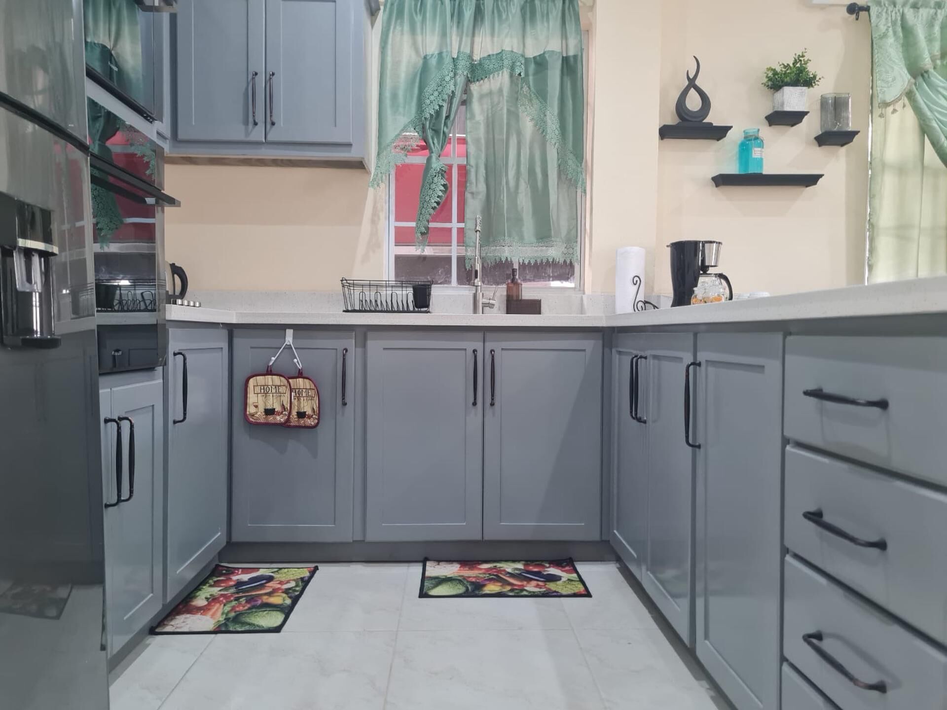 A kitchen with grey cabinets, a sink, a coffee maker, and a window with curtains.