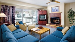 Una sala de estar con un sofá, televisión, chimenea y un balcón con cortinas.