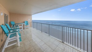 Un balcon avec des chaises turquoise et une table, donnant sur l’océan.