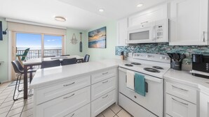 Une cuisine moderne avec des armoires blanches, un grand îlot central et une vue sur l’extérieur.