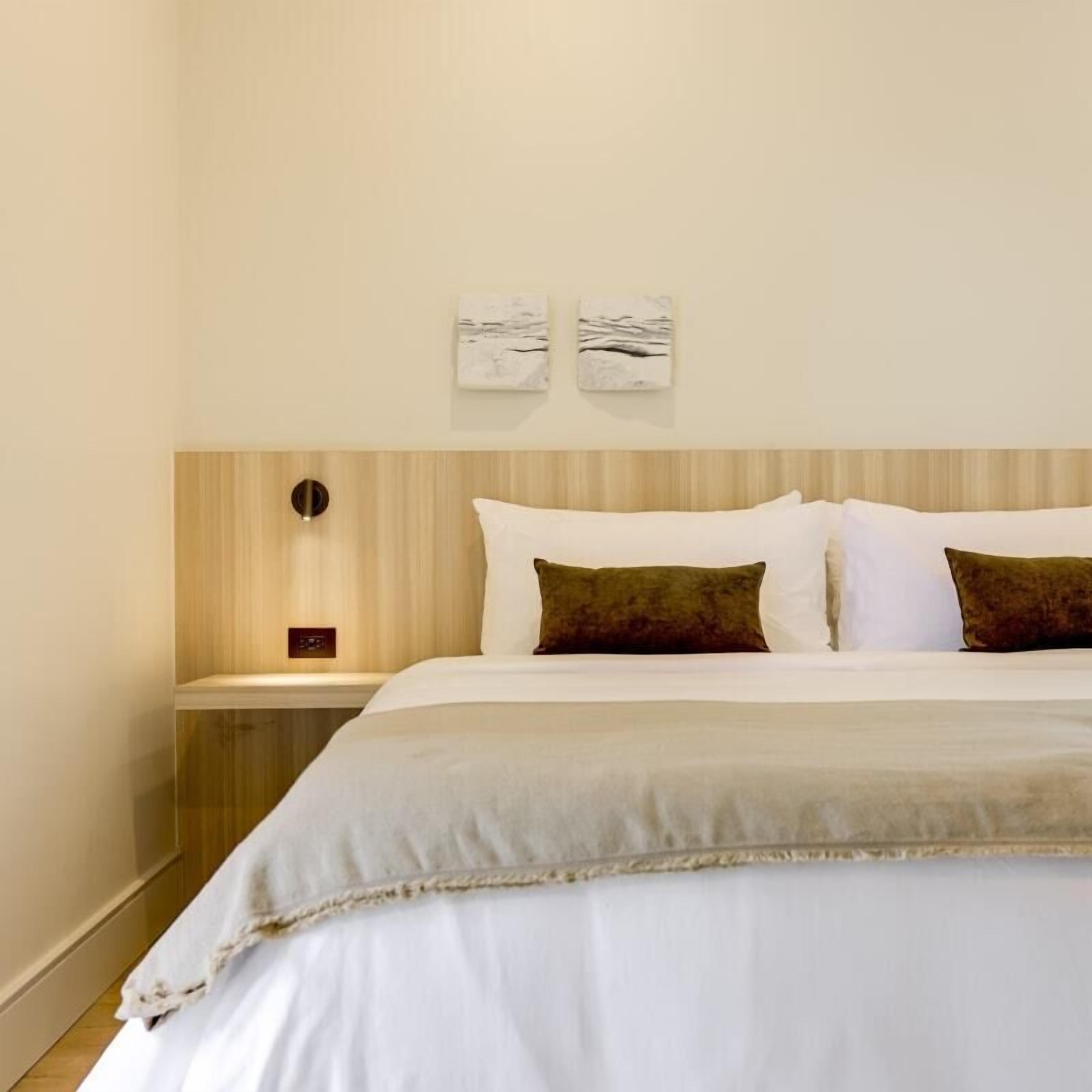 Een opgemaakt bed met witte en bruine kussens, een houten hoofdbord en twee kunstwerken aan de muur.