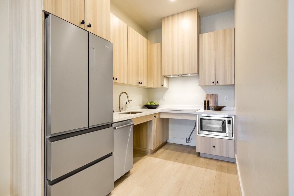 Una cucina moderna con mobili in legno chiaro, elettrodomestici in acciaio inossidabile e un piano di lavoro bianco.