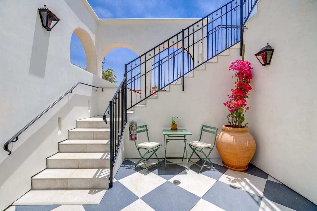 A staircase with a metal railing, a checkered floor, a table with chairs, and a large potted plant.