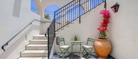 A staircase with a metal railing, a checkered floor, a table with chairs, and a large potted plant.