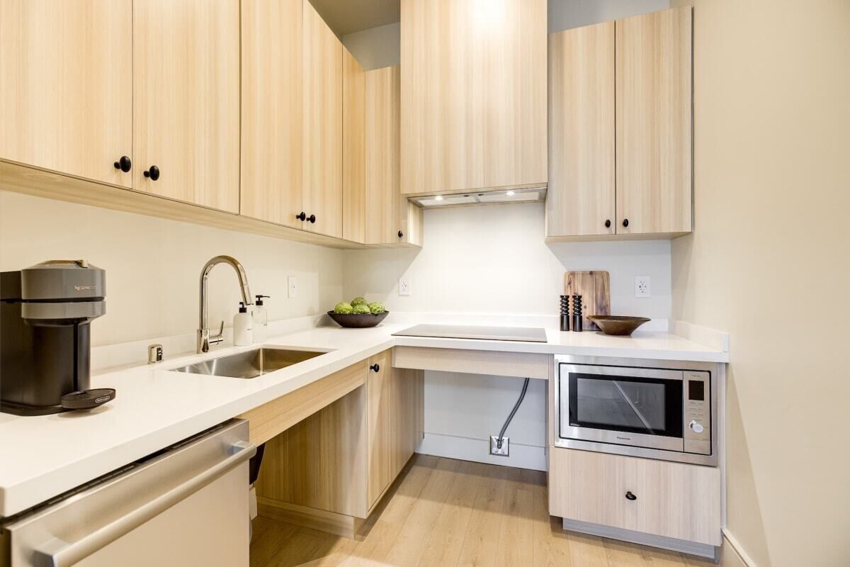 A compact kitchen with light wood cabinets, a built-in oven, a coffee maker, and a sink.