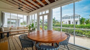 A spacious room with a wooden ceiling, large windows, a round wooden table, wicker chairs, and a bench with cushions.
