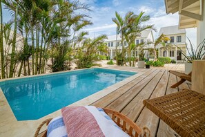Zona junto a la piscina con un muelle de madera, sillas de descanso y una piscina.