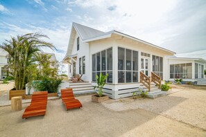 Una casa moderna con un gran ventanal, una escalera de madera y suelo arenoso.