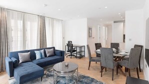 Un salon moderne avec un canapé bleu, une table basse en verre et un coin repas comprenant une table ronde et des chaises grises.