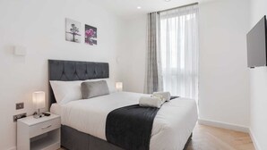 Une chambre moderne avec un grand lit, des tables de chevet, un téléviseur à écran plat et des œuvres d’art accrochées au mur.