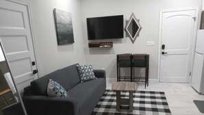 Ein Wohnzimmer mit einer Couch, einem Couchtisch, einem an der Wand montierten Fernseher und einem Schachbrettmuster-Teppich.