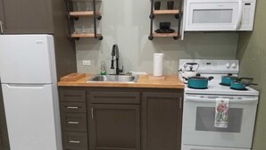 Eine kleine Küche mit Kühlschrank, Herd, Mikrowelle, Spüle und Holzregalen.