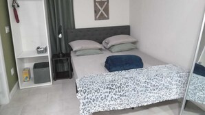Ein Schlafzimmer mit einem Bett, einem Kleiderschrank, einem Nachttisch und einem Fenster mit Holzrahmen.