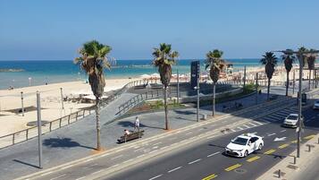 Una carretera costera con palmeras, una playa y un cielo azul despejado.