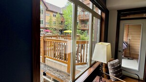 Ein Zimmer mit großem Fenster, Holzmöbeln und Blick auf einen Balkon mit Sitzgelegenheit.