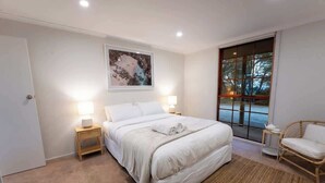 A bedroom with a large bed, bedside lamps, a window with a view, and a rattan chair. - Farm Stay, Picturesque views (Balhannah)