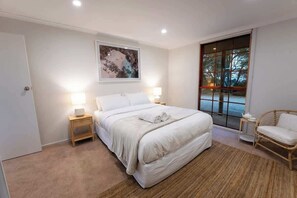 A bedroom with a large bed, bedside lamps, a window with a view, and a rattan chair. - Farm Stay, Picturesque views (Balhannah)