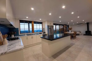 A modern kitchen with a large island, stainless steel appliances, and a view through large windows.