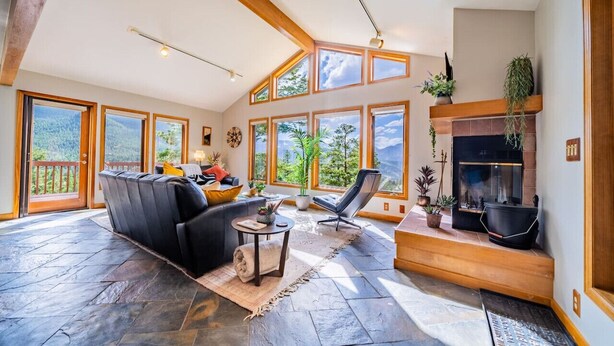 A spacious living room with a fireplace, large windows, and a stone floor.