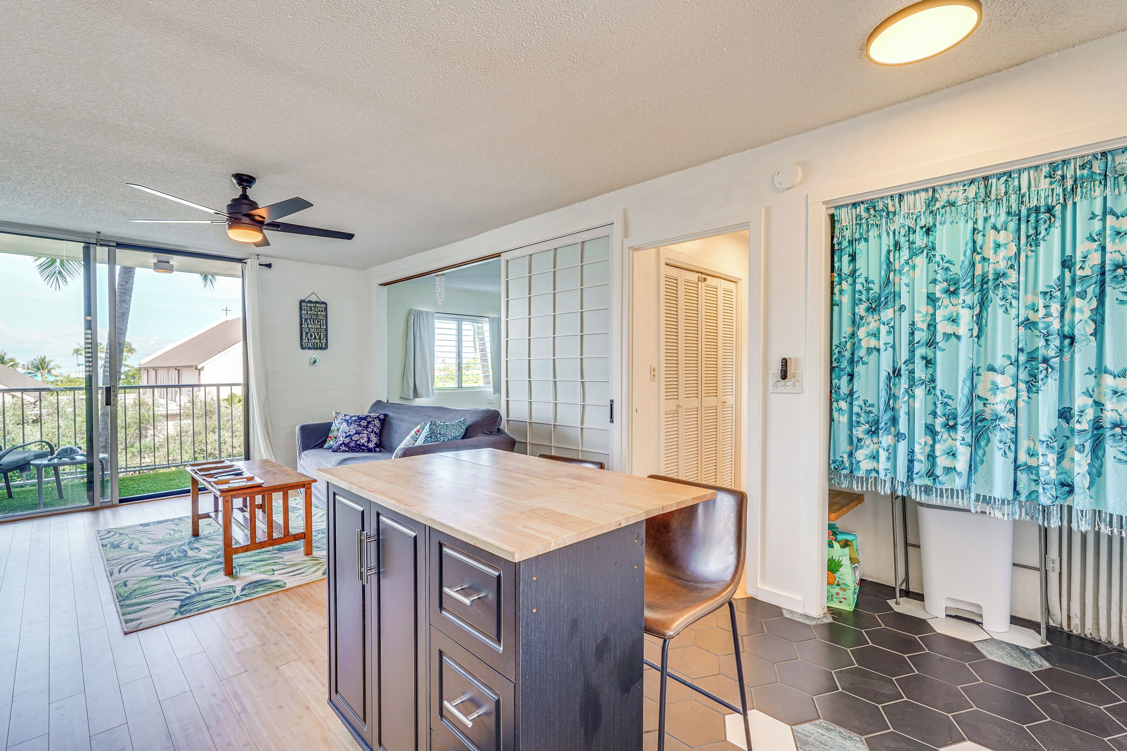 Une cuisine moderne avec un îlot central en bois, un ventilateur de plafond et une porte-fenêtre coulissante donnant sur un patio.